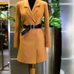 Sophisticated orange coat with belt displayed on a mannequin in an elegant setting.